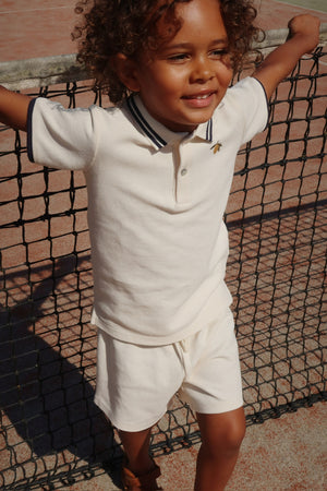 Smiling child in beige polo and shorts, enjoying outdoor play, showcasing comfortable and stylish summer clothing.