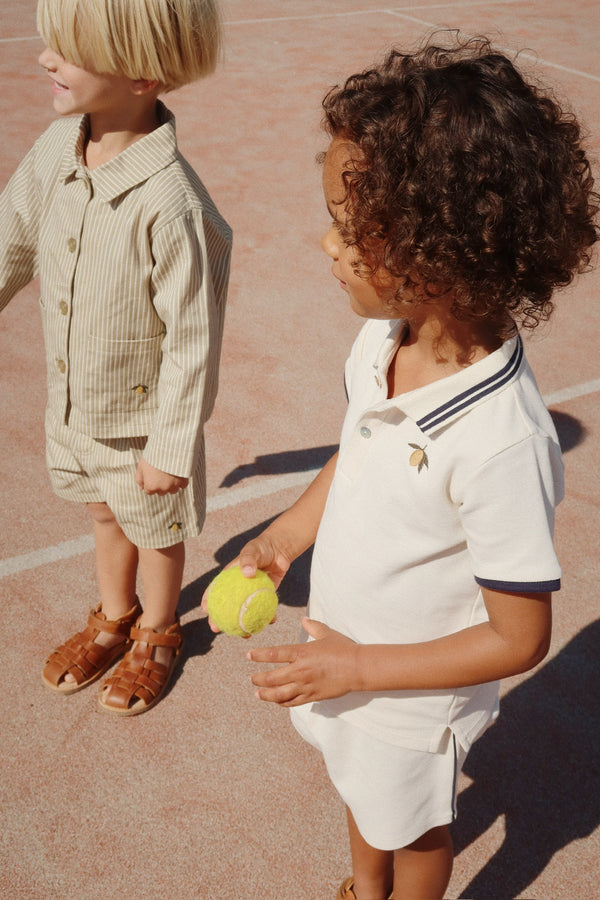 Two children in stylish outfits on a tennis court, featuring a white polo shirt and a striped shirt.