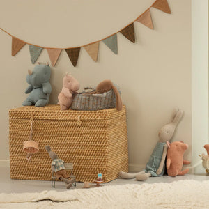 Colorful plush toys including rhinos and rabbits arranged around a woven basket in a cozy children's room.