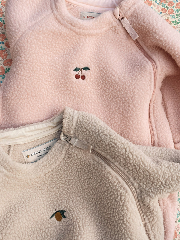 Two cozy fleece onesies in soft pink and cream, featuring cute embroidered fruit designs for babies.