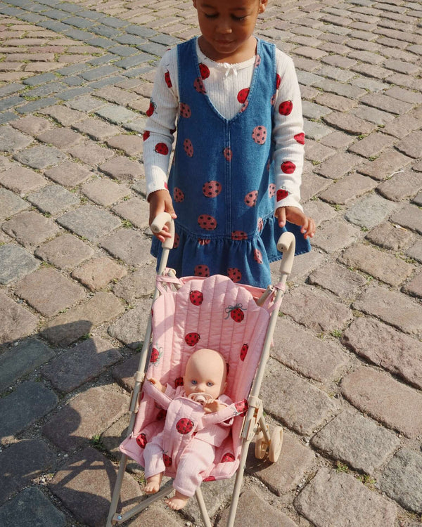 Child pushing a ladybug-patterned doll stroller with doll on cobblestone path.