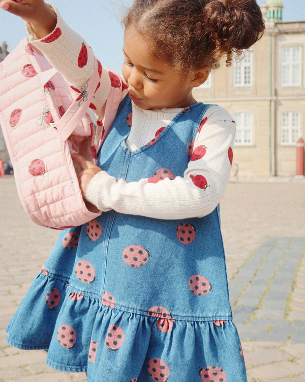 Child wearing a ladybug-themed dress and holding a matching quilted bag outdoors.