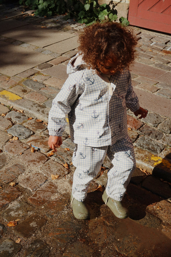Child wearing Palme Regenset Sailor Check outdoors, exploring in a waterproof outfit with anchors on a cobblestone path.