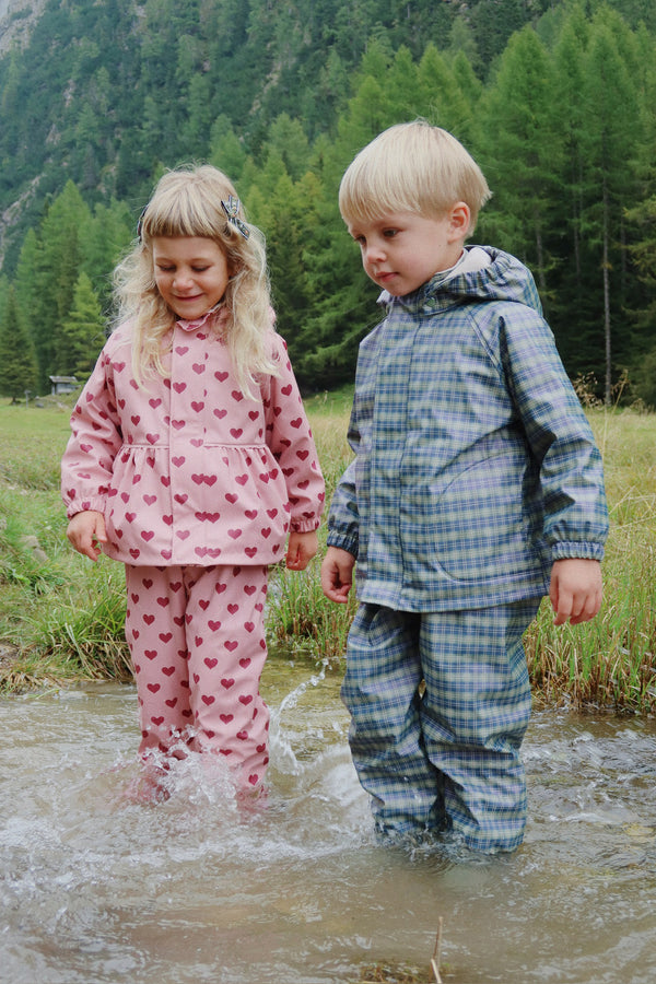 Zwei Kinder in wasserfesten Regensets spielen im Wasser, geschützt und glücklich bei schlechtem Wetter.