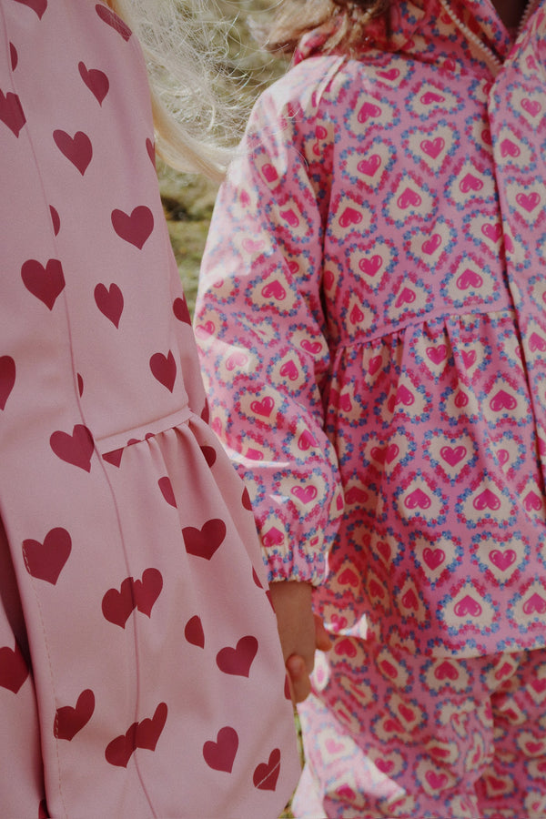 Zwei Kinder in farbenfrohen Regenjacken mit Herzmotiven, ideal für Abenteuer bei jedem Wetter.