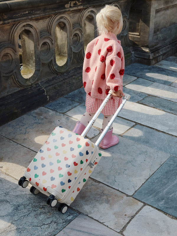 Child pulling a colorful heart-patterned suitcase from Konges Slojd while wearing a stylish outfit.