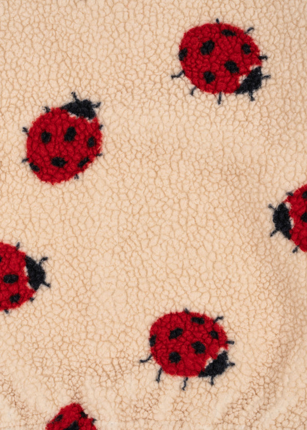 Close-up of Jody Teddyjacke fabric featuring red ladybug patterns on soft beige fleece.